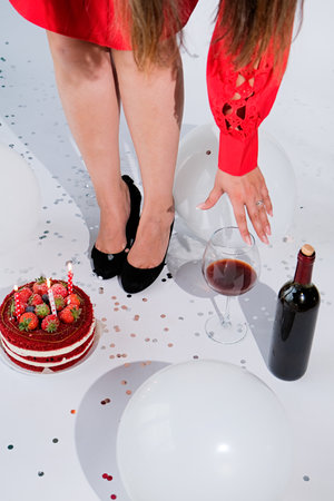 top down view of female legs red dress and back shoes celebrating birthday, red velvet cake, wine and confetti. Holiday Celebration, Joyful Events Concept, partyの写真素材