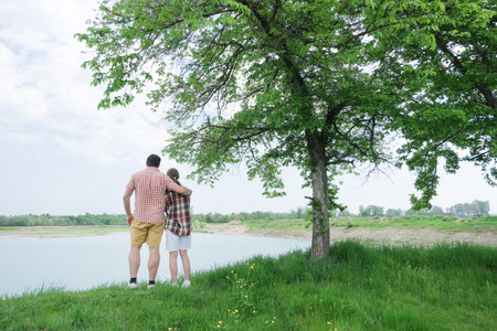 Family on picnic near the lake, standing on grass and hugging, looking at viewの写真素材