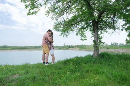 Family on picnic near the lake, standing on grass and hugging, looking at view