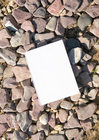 A blank white book or notebook resting on stones with natural sunlight. A serene and minimalist design conceptの写真素材