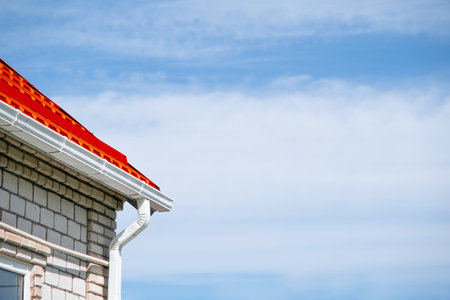 Rain Gutter Pipeline System on brick house, bright red metal tile roof against blue sky