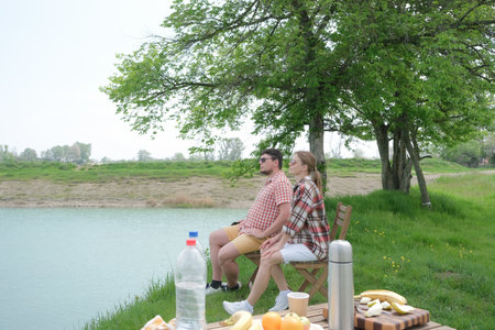 Family on picnic near the lake, sitting on chairs, looking at viewの写真素材