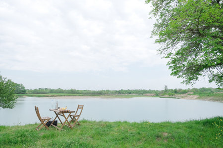 picnic near the lake, wooden furniture table and chairs with food near lakeの写真素材