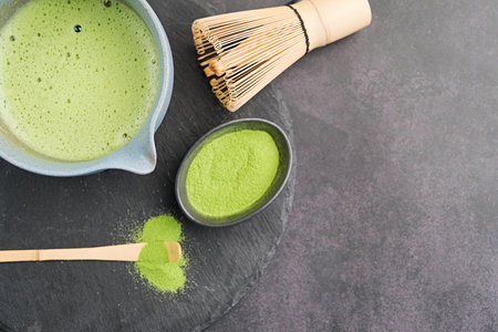 Traditional Japanese green matcha kit, bamboo whisk and beverage on slate plate, dark background...