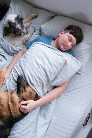 life with pets. Young millennial man sleeping lying in the bed in the morning with dogsの写真素材