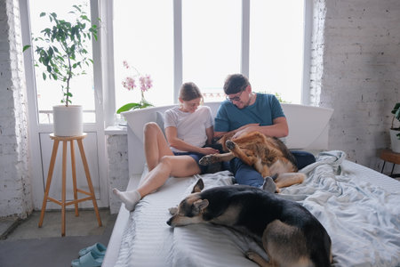 Life with pets. happy young millennial couple having breakfast in bed and enjoying fun time with their dogの写真素材