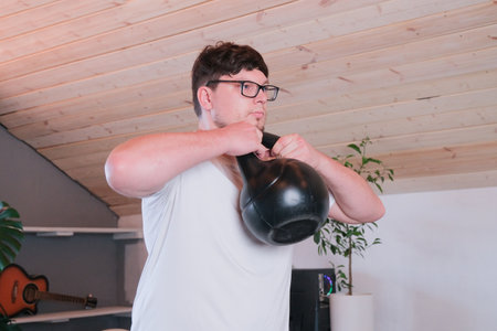 man training with kettlebell at home while working from the computer from home, performing workout between working sessionsの写真素材