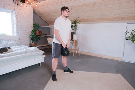 man training with kettlebell at home while working from the computer from home, performing workout between working sessionsの写真素材