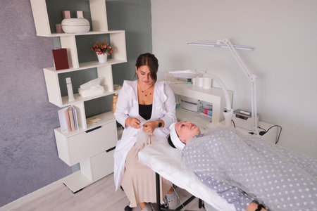 A cosmetologist preparing to make cleaning procedures to a client in a beauty salon, adjusting lamp and disinfecting handsの写真素材
