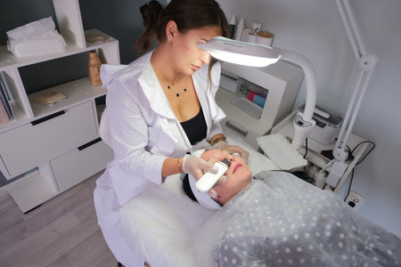 professional ultrasound cleaning appliance in hands of a cosmetologist cleaning face of female client. Ultrasound skin cleaning in modern health and beauty salonの写真素材