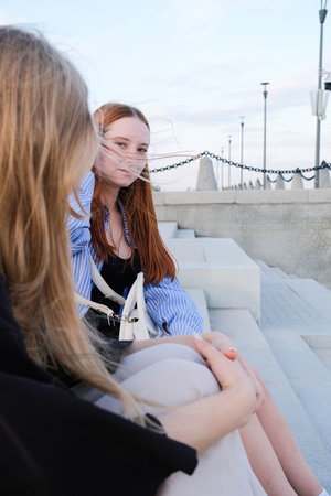 two female friends sitting on the stairs looking at the river at sunset sky