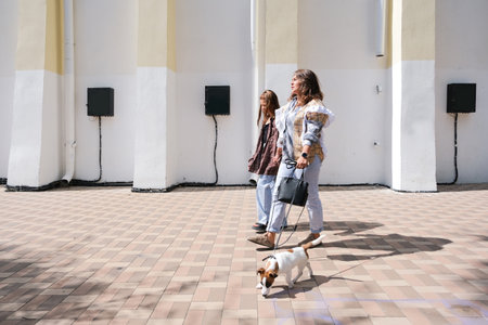 young woman and her daughter walking her terrier puppy in the city parkの写真素材
