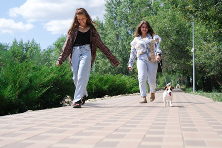 young woman and her daughter walking her terrier puppy in the city parkの写真素材