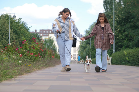 young woman and her daughter walking her terrier puppy in the city parkの写真素材