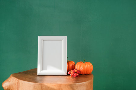 minimal autumn composition with white frame mockup and pumpkins over dark green wall background