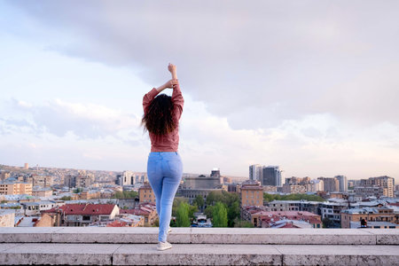 Young female tourist enjoys the view of Yerevan city at sunset. back view. Lifestyle, travel,...