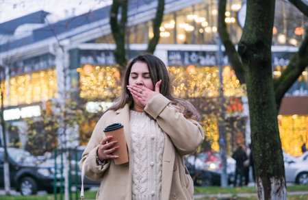 young woman standing outdoors on night neon street cafe illuminated for new year, drinking coffee to...
