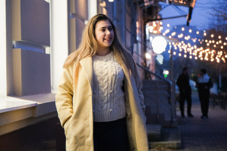 young woman standing outdoors on night neon street cafe illuminated for new year, drinking coffee to goの写真素材