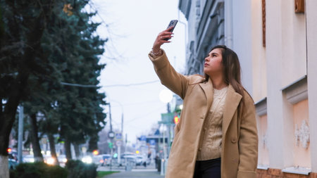 young woman standing outdoors on night neon street illuminated for new year holding smartphoneの写真素材