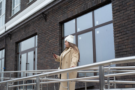 woman wearing warm coat standing at staircase at apartment building holding handrails. Casual, urban, minimalist, youth, outdoor, fashion, lifestyleの写真素材