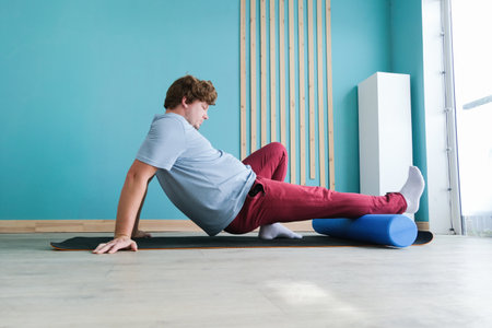 sportive man training using mfr or massage roll at home. Caucasian man doing exercises using large...