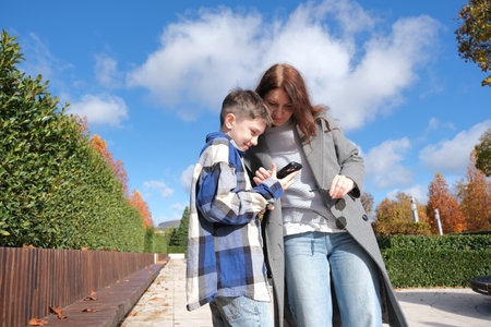 mother and son putting on sunglasses in the street taking photos on the phone and looking at the screenの写真素材
