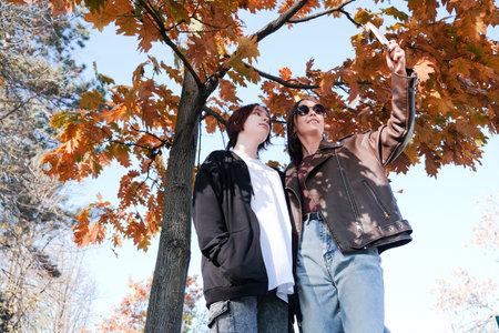happy mother with her daughter walking in autumn park, taking selfie under yellow tree