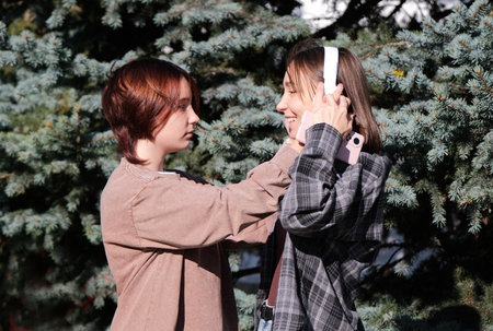 mother and teen daughter listening to music outdoors, girl putting headphones on motherの写真素材