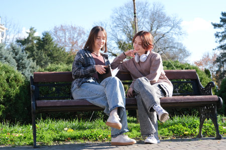 teen girl and mother sitting on a park bench reading notes in a notebookの写真素材