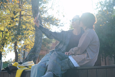 teen girl and mother sitting on a park bench using smartphoneの写真素材