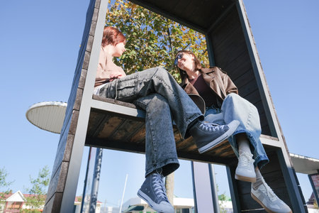 teen girl and mother sitting on a park bench talking and laughing, view from belowの写真素材