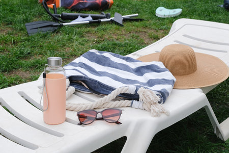 beach accessories with beach bag, hat, sunglasses and water bottle on the lounge over green grassの写真素材