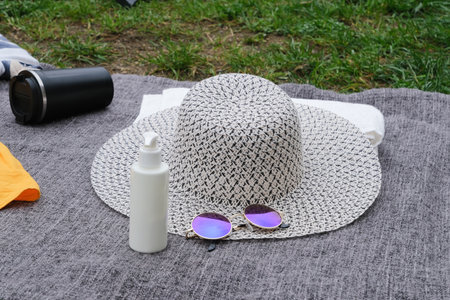 beach accessories with beach bag, hat, sunglasses and sunscreen bottle on the blanket over green grassの写真素材