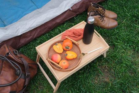 low canping table with persimmon fruit and drink near camping tent