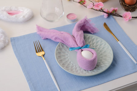 Easter table setting, egg with bunny ears on plate on the table decorated for Easter, high angle...