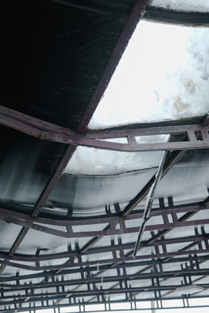 Broken polycarbonate roof with cracked metal farms and cut holes. Bent metal construction of...