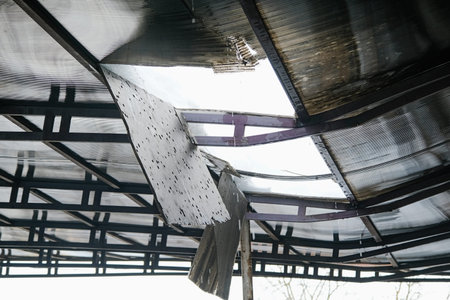 Broken polycarbonate roof with cracked metal frames and cut holes. Bent metal construction of...