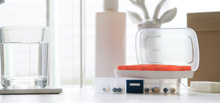 Plastic pill organizers, blisters of pills and glass of water on table