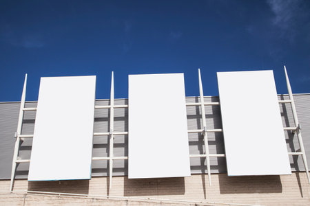 Three blank billboards on a building wall with blue sky in the background