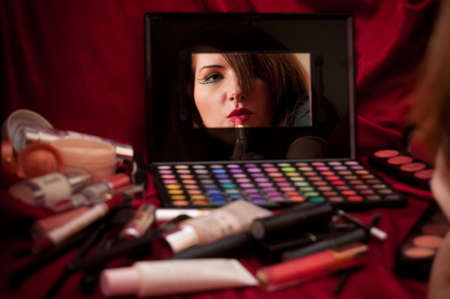 Woman in mirror applying makeup. Red background.の写真素材