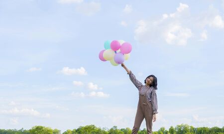 Asian girl holding colorful balloons with blue sky background.