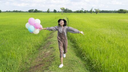 Asian young girl holding balloon running at beautiful field rice, Nature background.の写真素材