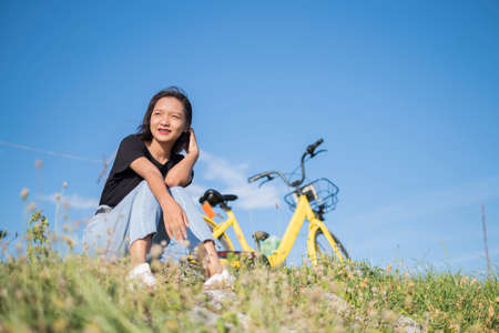Happy young asian girl with yellow bicycle at park .