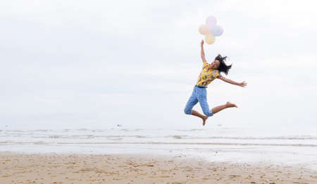 Asian young girl jumping and hold balloon at the beach.の写真素材
