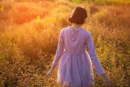 Young girl standing at brown field grass at sunset time.の写真素材