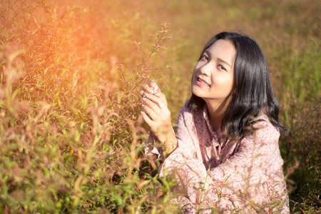 Beautiful young girl wear pink dress sitting at field grass with happy emotion.の写真素材