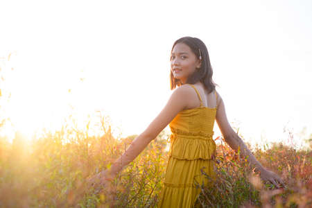 Young girl standing at brown field grass at sunset time.の写真素材