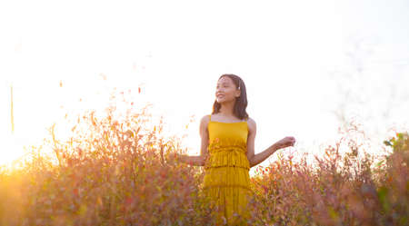 Young girl standing at brown field grass at sunset time.の写真素材