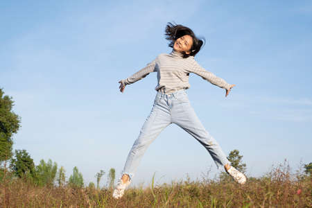 Young girl jumping at field grass with blue sky.の写真素材