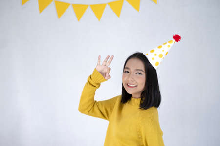 Beautiful girl wear yellow sweater, party hat and smiling, white backdrop.
